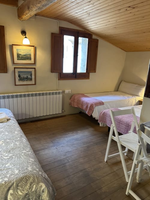 Dormitorio L'Esquirol en Casa Tapiolas de Molló con vigas de madera, múltiples camas, radiador y vistas a la montaña