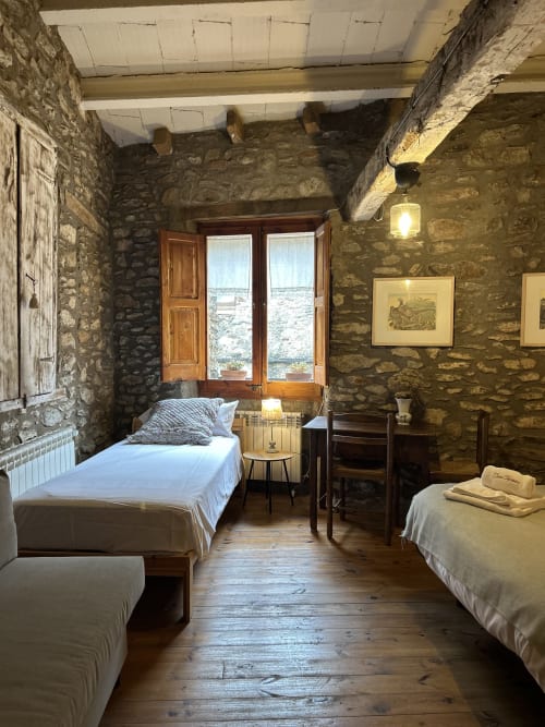 Dormitorio rústico de piedra en Casa Tapiolas en Molló con dos camas, vigas de madera y puertas con vistas a las montañas