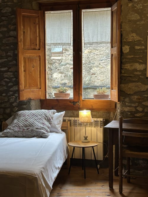Acogedor dormitorio en Casa Tapiolas de Molló con muros de piedra, puertas de madera hacia vistas y mobiliario sencillo