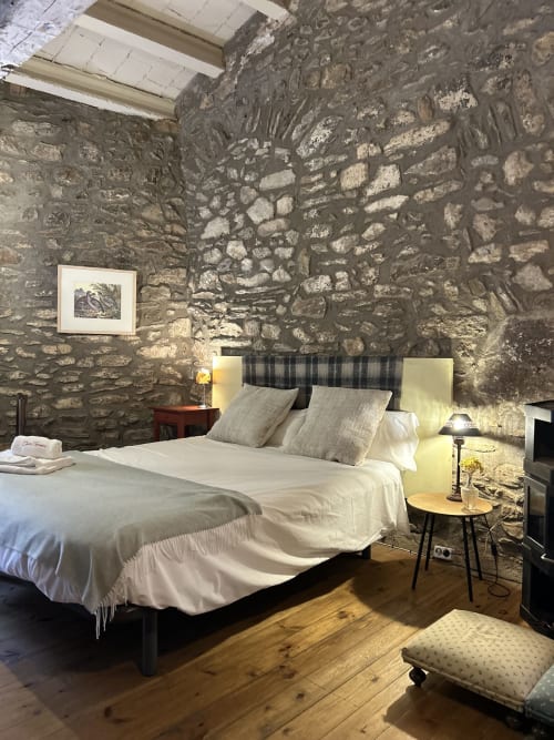 Dormitorio rústico en Casa Tapiolas en Molló con paredes de piedra, ropa de cama blanca, suelo de madera e iluminación ambiental