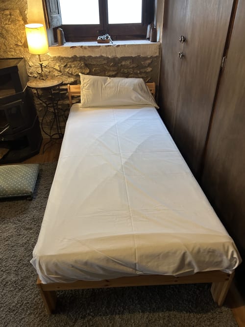 Cama individual con sábanas blancas en la habitación Mussol de Casa Tapiolas, Molló Girona, con pared de piedra y ventana