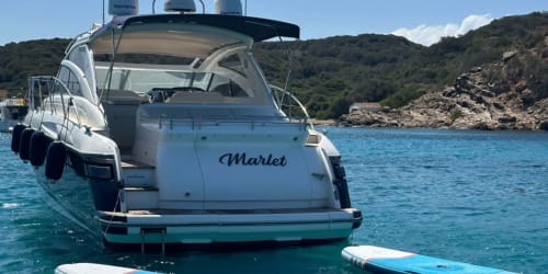 Yate de lujo 'Marlet' fondeado en aguas turquesas cerca de Cap d'Artrutx con costa rocosa y colinas frondosas.