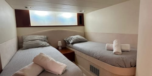 Cabaña con habitación doble en Las Golondrinas con dos camas individuales, ropa de cama a rayas y ventana de ojo de buey en Cap d'Artrutx