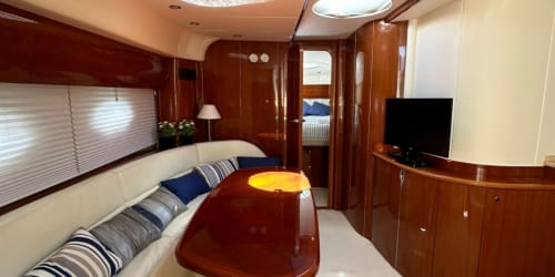 Salón de lujo de yate con panelado de madera noble, tapicería color crema y mesa redonda en Las Golondrinas Cap d'Artrutx