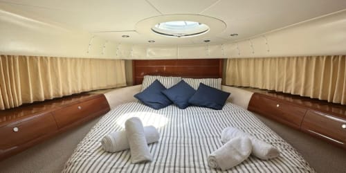 Dormitorio principal de lujo en yate con ropa de cama a rayas, almohadas azules y cortinas crema en Las Golondrinas, Cap d'Artrutx