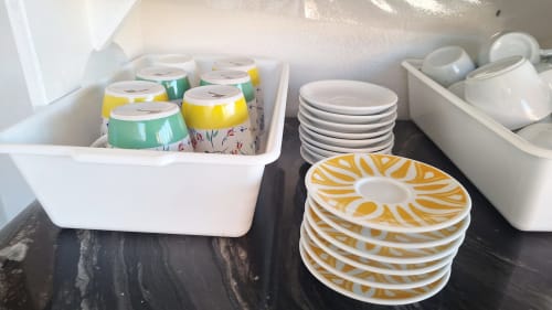 Armadio della cucina a B&B Villa Matari con contenitori bianchi ordinati, tazze colorate, piatti impilati e stoviglie