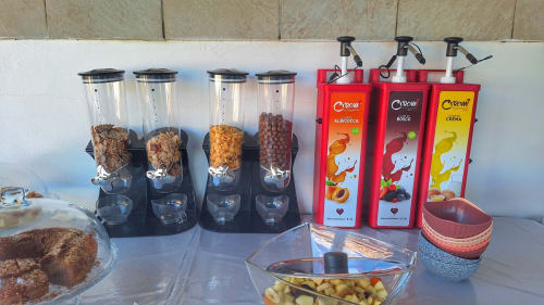 Stazione colazione presso B&B Villa Matari con dispenser di cereali, sciroppi, pasticceria e ciotole a Fontane Bianche