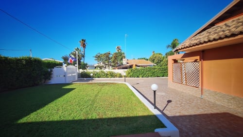 Patio de la Villa Matari con jardín cuidado, edificio de terracota y palmeras en Fontane Bianche, Sicilia