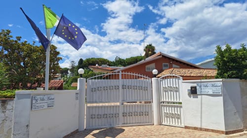 Cancello d'ingresso di B&B Villa Matari con bandiera dell'UE a Fontane Bianche, Sicilia, con muri bianchi e tetti in terracotta