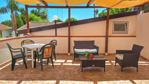 Area terrazza presso B&B Villa Matari a Fontane Bianche con tavolo da pranzo e sedie a sdraio sotto baldacchino giallo