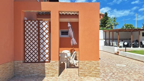Cortile di Villa Matari con edificio in terracotta, porta a grata e sedute in patio a Fontane Bianche, Sicilia