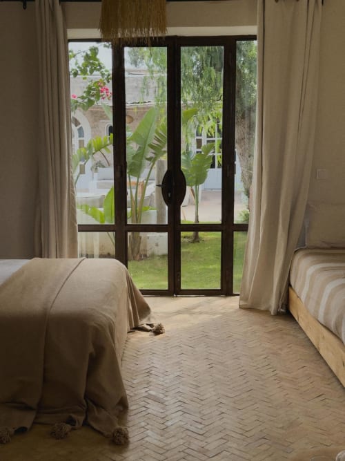 Interior de una habitación con decoración bohemia, suelo de bejmat y puerta de forja con vista a la piscina en un riad en Essaouira