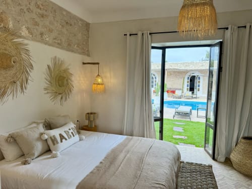 Una habitación con decoración bohemia, tejidos de lino, suelo de bejmat, cestas de mimbre y luminaria con vista a la piscina en el Riad Eucalyptus en Essaouira
