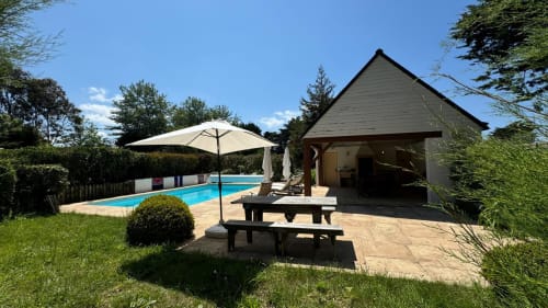 Cottage au bord de la piscine à Loc'Maria Belle Île en Mer avec parasol, table de pique-nique et pergola moderne surplombant la piscine bleue