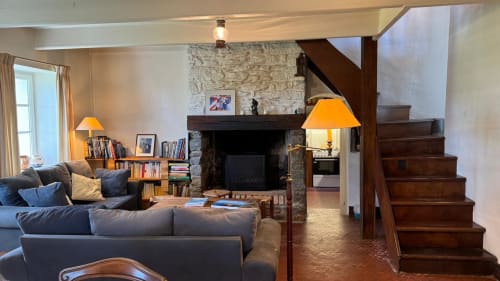 Salon cosy du gîte Locmaria Belle Île avec cheminée, escalier en bois, sièges confortables et bibliothèques.