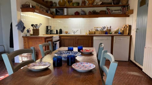 Coin repas du gîte Loc'Maria Belle Ile avec table en bois, chaises bleues, couverts et cuisine équipée blanche