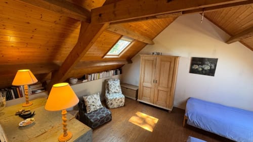 Chambre mansardée chaleureuse avec poutres apparentes, deux lampes, fauteuils, penderie et lit bleu dans un gîte de Belle-Île-en-Mer