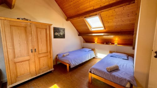 Chambre douillette sous les toits avec deux lits jumeaux, poutres en bois, lucarne et éclairage chaleureux au gîte Locmaria