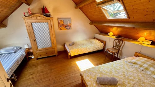 Chambre lumineuse sous les toits du gîte Loc'Maria à Belle Île avec plafond en bois, trois lits, armoire en bois et puits de lumière