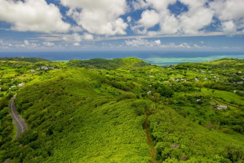 Versant verdoyant dominant une lagune turquoise et l'océan, île Rodrigues avec route sinueuse et maisons dispersées