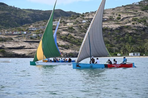 Deux bateaux à voiles colorés avec passagers près de la plage de l'île Rodrigues, eau cristalline et maisons du village accrochées à la colline