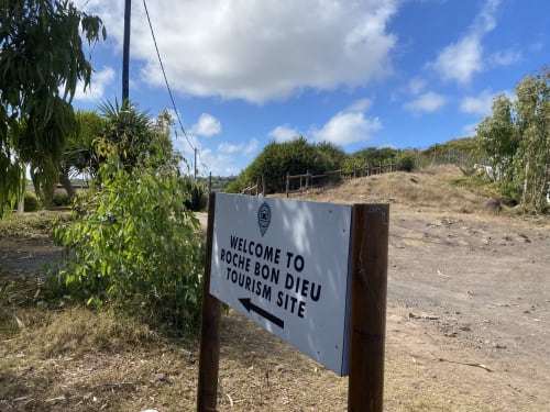 Panneau d'accueil du site touristique Roche Bon Dieu à Rodrigues avec végétation tropicale et ciel bleu