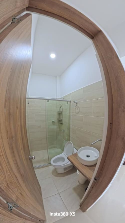 Baño moderno en Olamar Living, Coveñas, con ducha de vidrio, inodoro, lavamanos y marco de puerta en madera
