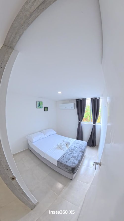 Moderno dormitorio en Olamar Living de Coveñas con cama blanca, aire acondicionado y cortinas oscuras con vista a la piscina