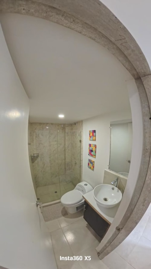 Baño moderno en Olamar Living de Santiago de Tolú con inodoro, lavamanos redondo, ducha de cristal y arte mural colorido