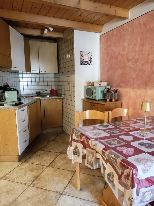Zona cucina e pranzo in monolocale ad Al Dos a Livigno con arredi in legno, tovaglia a fantasia rossa e vista montagna