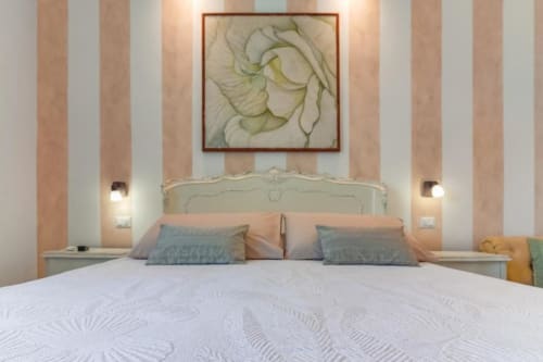 Elegant bedroom at Alghero Roof Garden B&B with striped walls, ornate headboard, and floral artwork