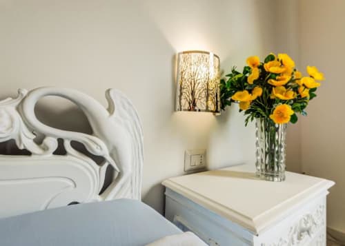 Bright bedroom with yellow flowers in vase, wall sconce, and white ornate furniture at Alghero Roof Garden B&B
