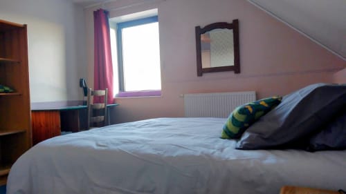 Bright bedroom with white bed, colorful pillows, wooden furniture, and garden view window at Au Coeur des Champs B&B in