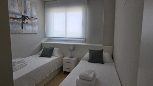 Dormitorio doble moderno con camas blancas, almohadas oscuras y vistas al jardín en el apartamento MiramaRent de Benicàssim
