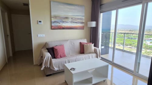 Salón moderno con sofá beige, mesa de centro blanca y amplio balcón con vistas a los jardines de Benicàssim