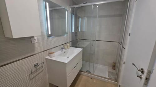 Baño moderno en apartamento MiramaRent, Benicàssim con vanidorio blanco, amplia ducha y azulejos de rayas