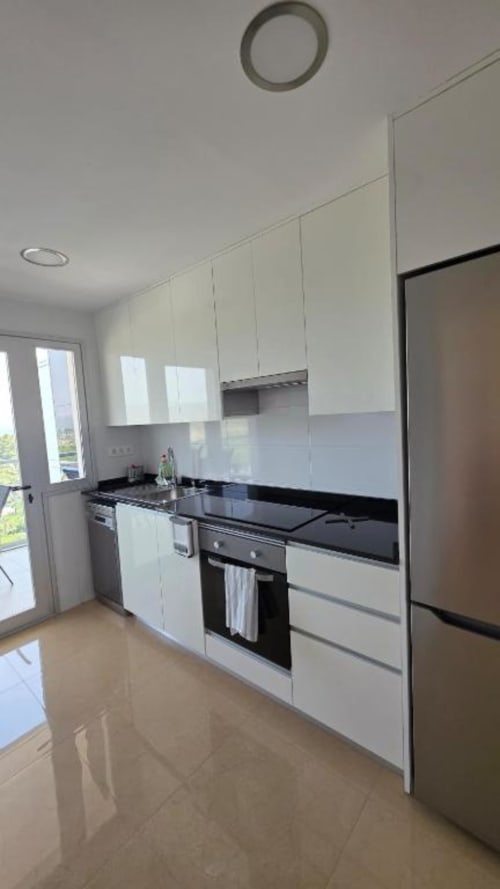 Cocina moderna en apartamento de Benicàssim con armarios blancos, encimeras negras, electrodomésticos de acero inoxidable y vistas al jardín