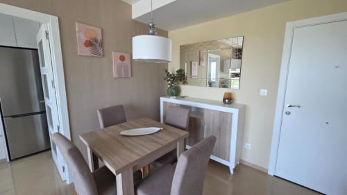 Comedor de apartamento moderno con mesa de madera, sillas tapizadas, cocina de acero inoxidable y muebles contemporáneos