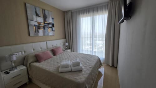 Dormitorio moderno en apartamento MiramaRent con balcón vista al mar, ropa de cama beige, almohadas rosas y arte contemporáneo