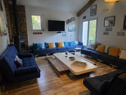 Großzügiges Wohnzimmer des Cottage Le Manoir Lacustre mit blauer Bestuhlung, Holztisch, TV, Kamin und Gartenblick