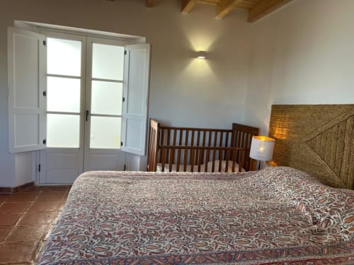 Quarto luminoso da villa Casa dos Queixos em Marvão com berço de madeira, roupas de cama estampadas e portas francesas com vista para a montanha
