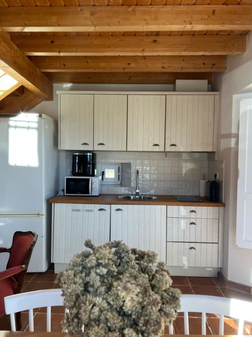 Cozinha clara com armários brancos, vigas de madeira e bancadas marrom na villa Casa dos Queixos em Casas de Juromenha