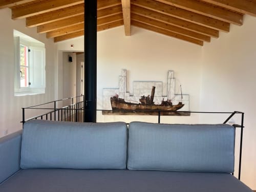 Quarto moderno com cama estofada em azul, vigas de madeira aparente, arte náutica rústica, corrimão metálico e grande janela na Casa