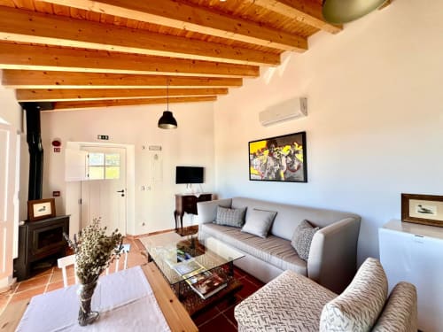 Espaçosa sala de estar da villa Casas de Juromenha em Marvão com vigas de madeira aparentes, sofá cinzento, TV e estilo tradicional