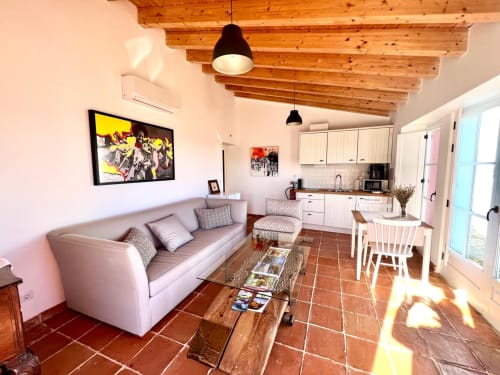 Espaço de estar moderno e luminoso em Casas de Juromenha com tetos de vigas, sofá cinzento, cozinha e pisos em terracota