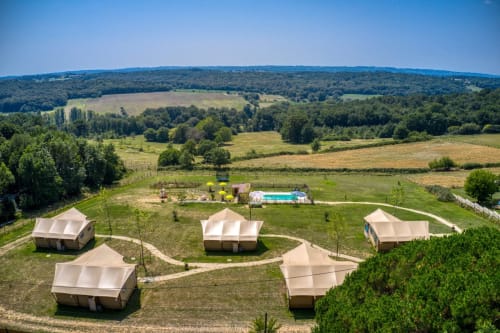 Vue aérienne des tentes glamping de Home Sweet Lodge en Aquitaine, avec des champs verdoyants et des collines ondulantes.