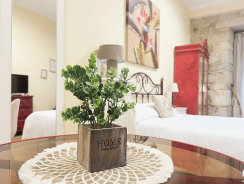 Dormitorio del apartamento Vermello en Baiona con cama doble, acentos rojos, planta verde sobre mesa y vistas a la ciudad