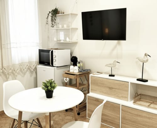 Moderno apartamento estudio en Baiona con mesa de comedor redonda, TV de pantalla plana, microondas y muebles de almacenamiento de madera en ambiente luminoso.