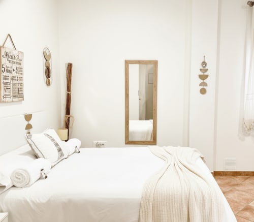 Dormitorio minimalista en el apartamento Ruliña, Baiona, con ropa de cama blanca, espejo de madera y decoración natural