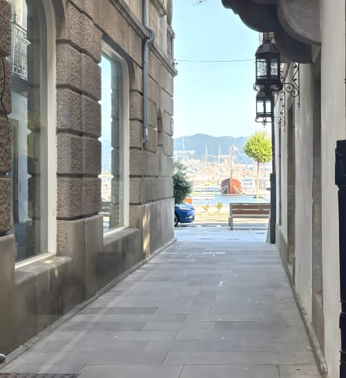 Estrecho callejón de piedra en Baiona que conduce a vistas de la marina con veleros y montañas